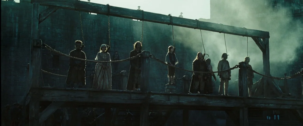 Pirates of the Caribbean: At World’s End movie still: wide — A wooden gallows structure stands before a large, weathered stone fortress wall.…