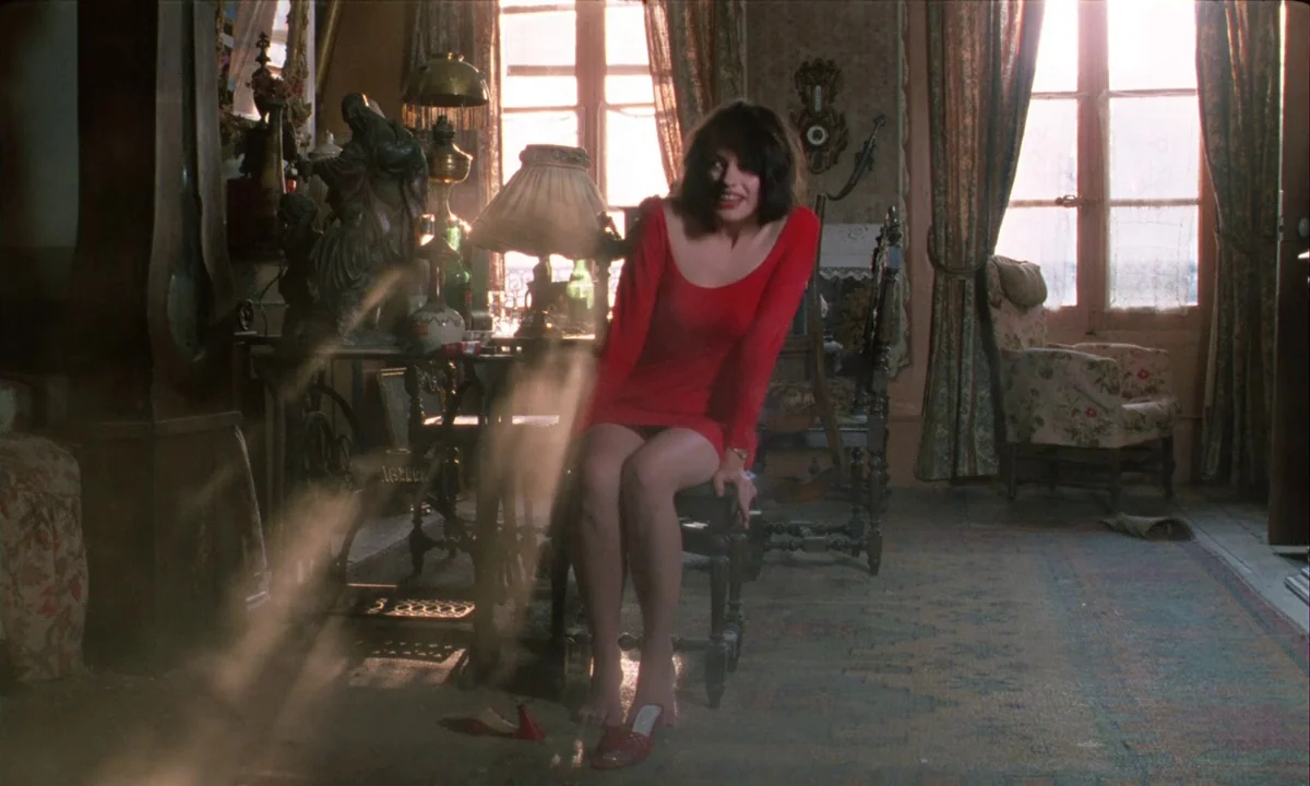 Betty Blue (1986) movie still: fullbody — A cluttered apartment room features lace curtains over sunlit windows and antique wooden furniture. A…