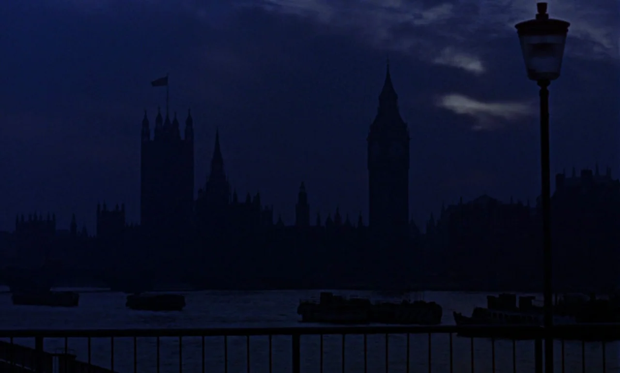 Dr. No (1962) movie still: establishing — The Houses of Parliament silhouette against a dark evening sky near the River Thames. A single streetlamp…