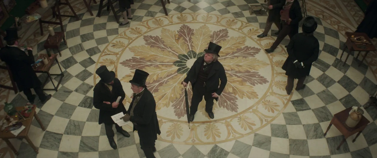 Mr. Turner (2014) movie still: wide — A spacious room with a prominent circular marble floor featuring floral motifs and checkered tiles. Several…