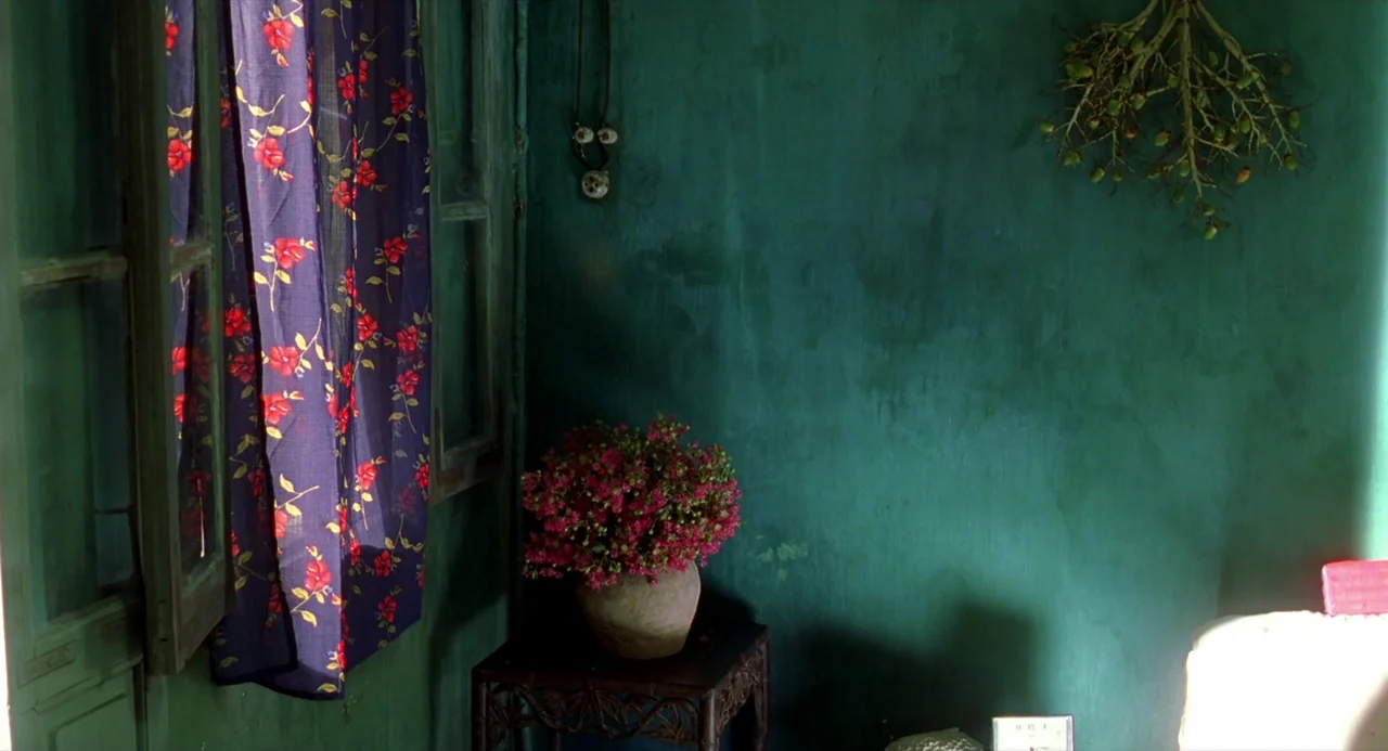 The Vertical Ray of the Sun (2000) movie still: wide — A teal-painted corner features an ornate side table holding a vase of pink flowers. An open…