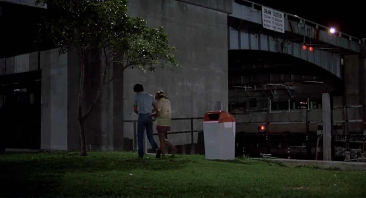 Harry and the Butler (1961) movie still: wide — A night scene under a concrete bridge shows a small tree and trash bin. A man and a woman walk away…