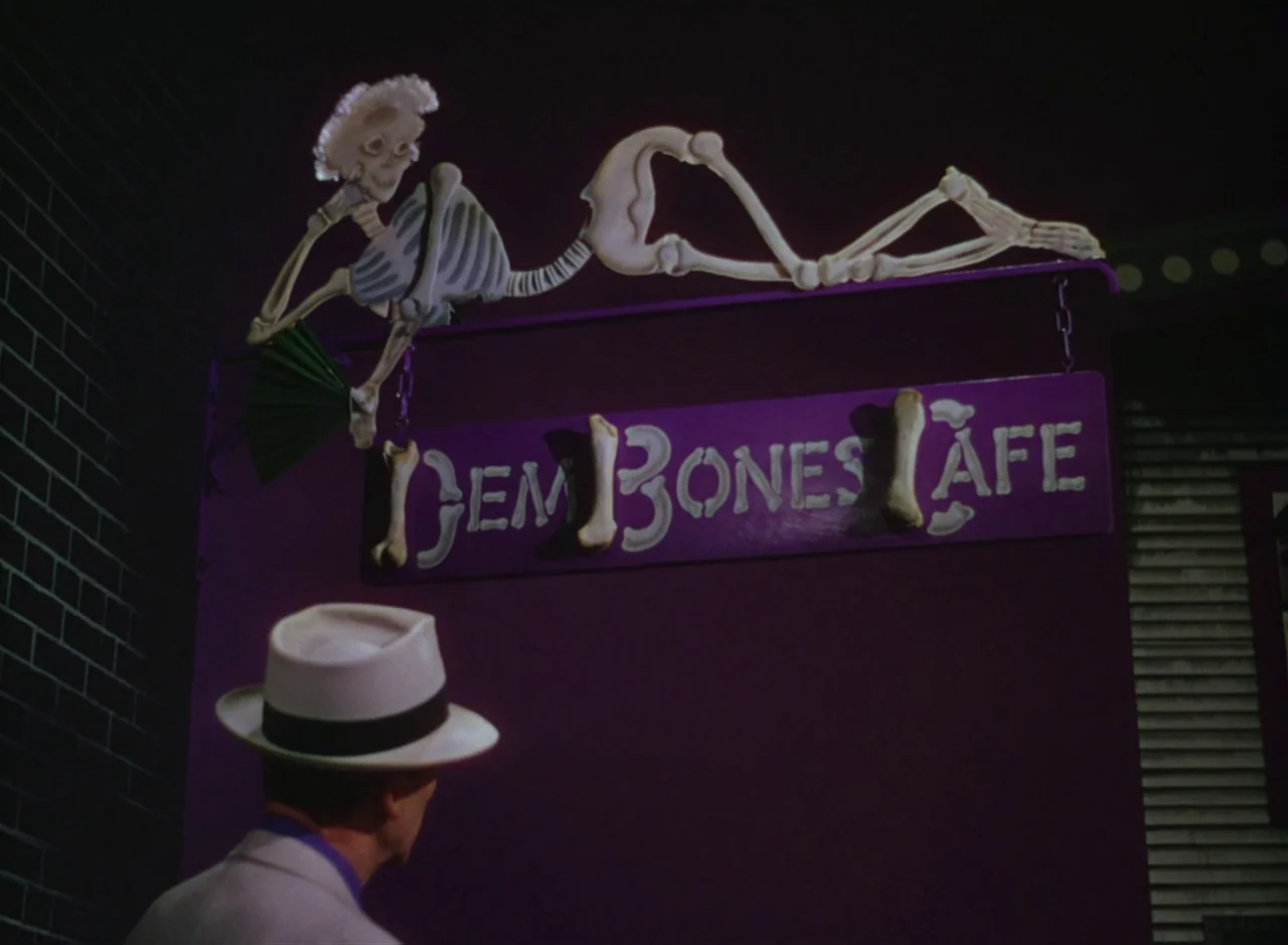 The Band Wagon (1953) movie still: medium — A dark night exterior displays a purple wall with a mounted Dem Bones Cafe sign. A man in a light suit…