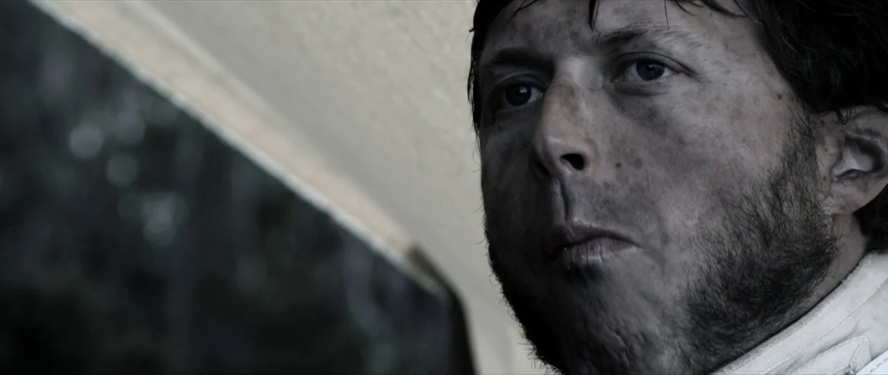 Van Diemens Land (2009) movie still: closeup — A man sits inside a vehicle with an out-of-focus background visible through the window. The subject…