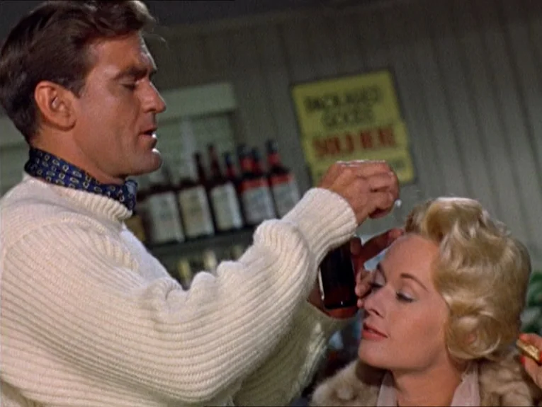 The Birds movie still: medium — A liquor store interior features shelves of bottles and a faded yellow product sign. A man in a cream sweater…