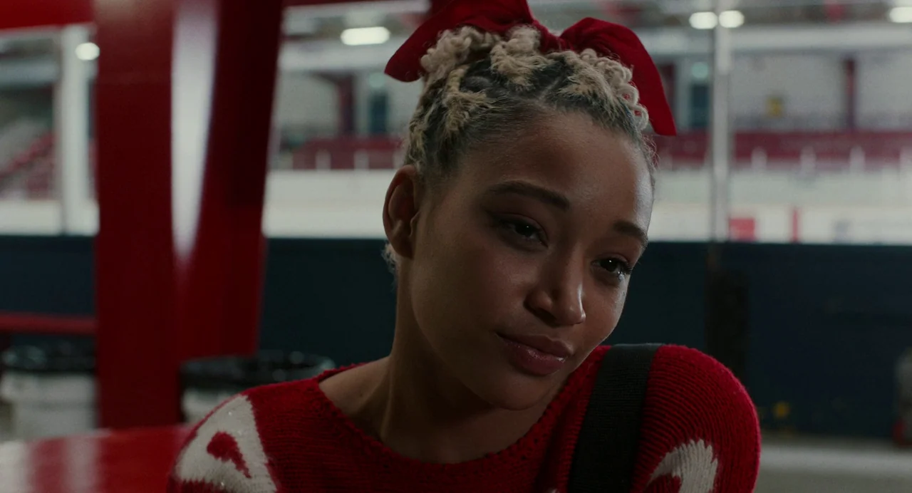 My Animal (2023) movie still: closeup — A woman stands in the interior of a large ice rink stadium. She is positioned in the foreground while empty…