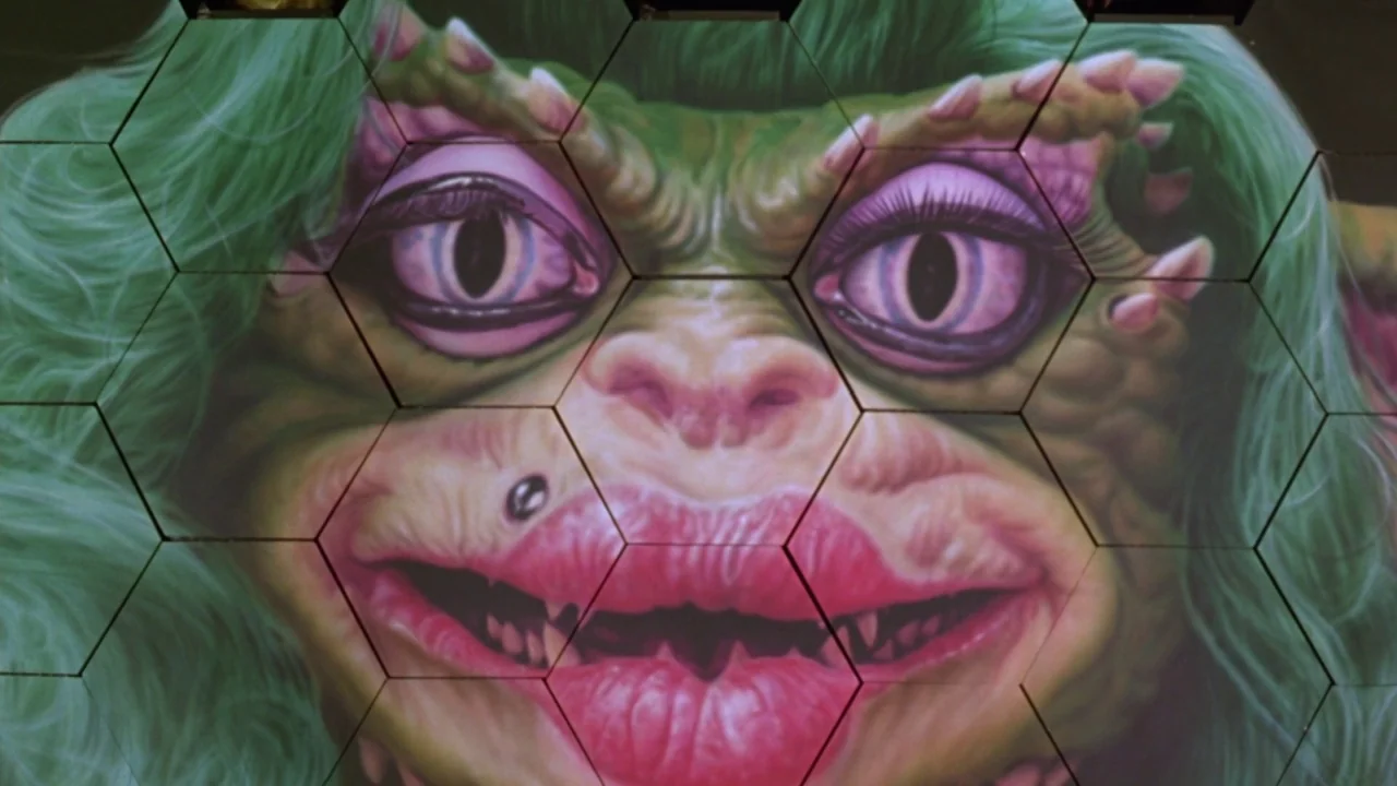 Gremlins 2: The New Batch movie still: closeup — A digital image of a Gremlin-like creature is projected onto hexagonal tiles. The creature features…