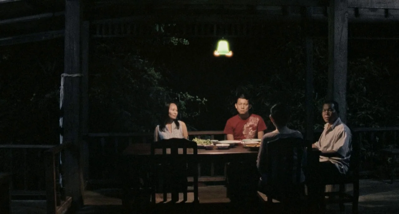 Uncle Boonme Who Can Recall His Past Lives (2010) movie still: wide — A wooden porch at night holds a table where four people sit in silence. Dark…