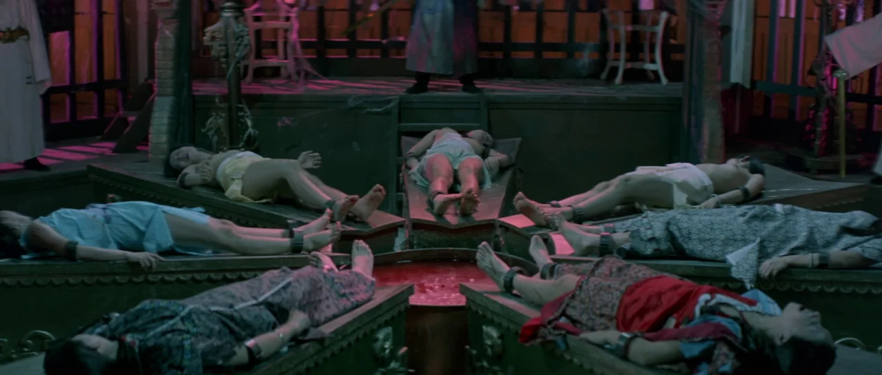 The Legend of the 7 Golden Vampires (1974) movie still: wide — A dark chamber features several people lying on individual stone slabs arranged in a…