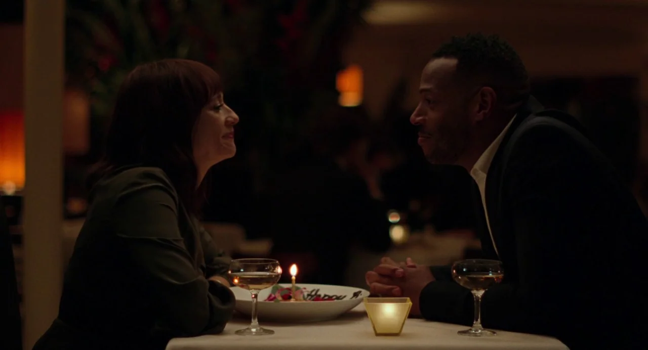On The Rocks (2020) movie still: medium — A dark restaurant interior features a table draped with a white cloth. A man and a woman sit opposite each…