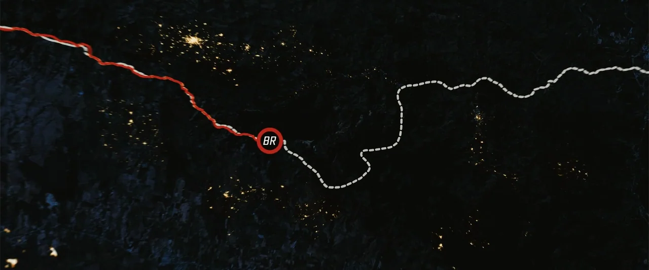Arthur the King (2024) movie still: establishing — A high-altitude satellite map of a landscape at night showing distant city lights. A bright red…