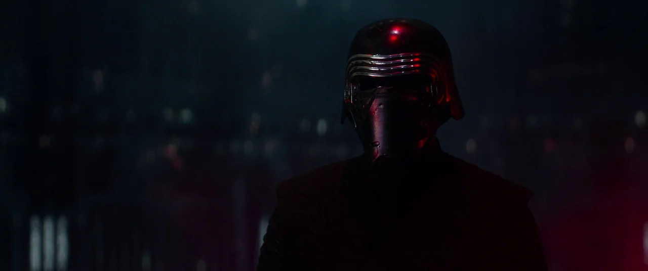 Star Wars: The Force Awakens (2015) movie still: medium — A dark, indistinct location with faint red glowing lights in the background. A figure…