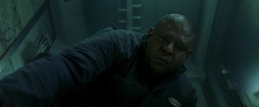 Panic Room (2002) movie still: medium — A narrow, dimly lit industrial corridor with metallic surfaces and green-tinted shadows. A middle-aged man…