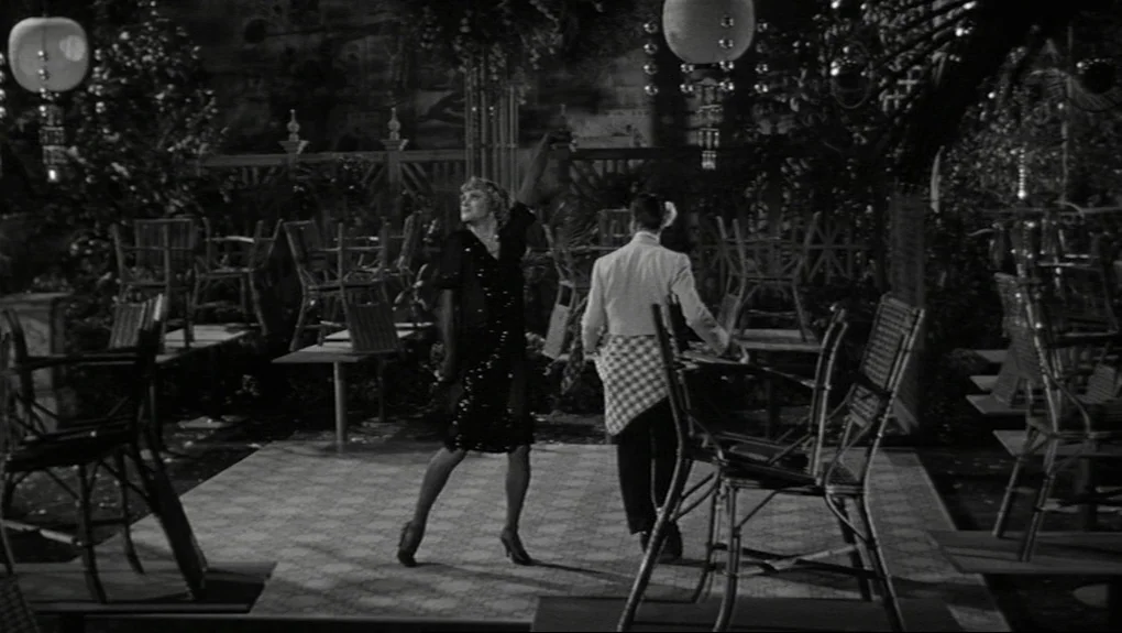 Some Like It Hot (1959) movie still: fullbody — An outdoor patio at night features numerous empty wooden tables and chairs arranged neatly. A woman…