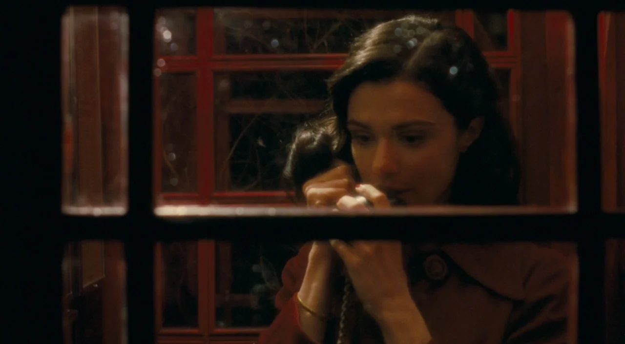 The Deep Blue Sea (2011) movie still: closeup — A classic red telephone booth structure is illuminated at night in darkness. A woman holds a…