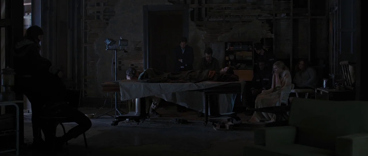 The East (2013) movie still: wide — A dark, dilapidated room with exposed wall studs and unfinished wooden surfaces. A group of survivors stands…