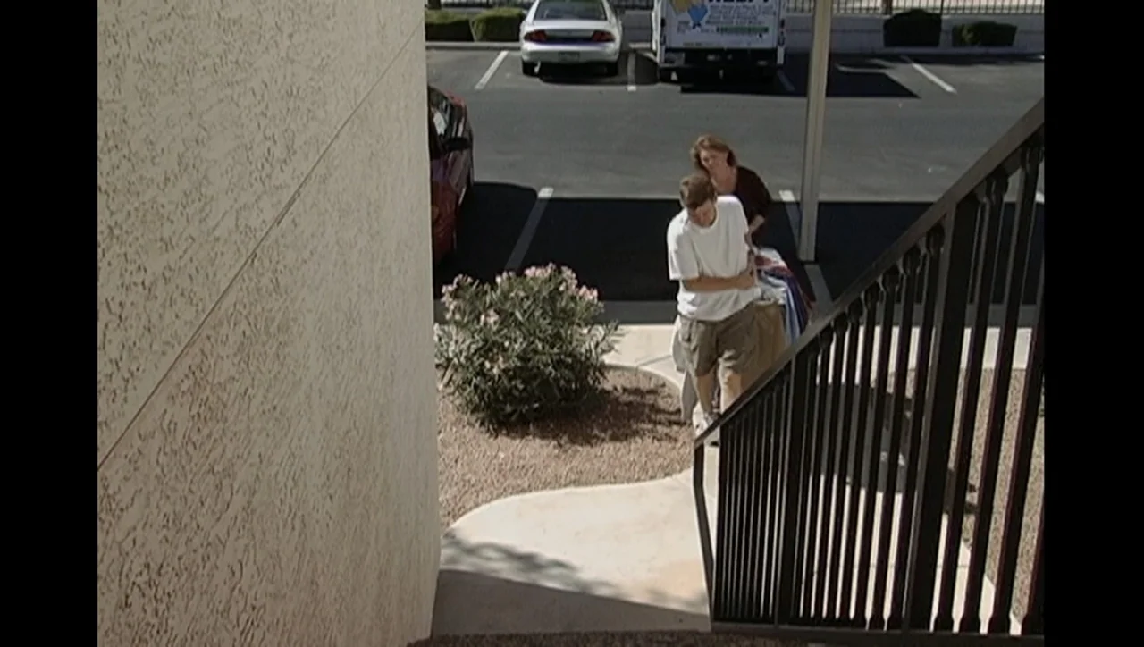 The Trials of Ted Haggard (2009) movie still: fullbody — A sunny outdoor parking lot adjacent to a beige building with stairs. A young man and an…
