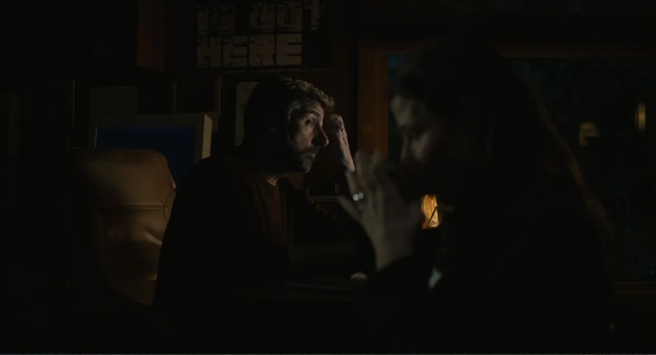 Beautiful Boy (2011) movie still: medium — A dark, cluttered home office contains a desk, computer monitor, and a wall poster. A man sits at his…