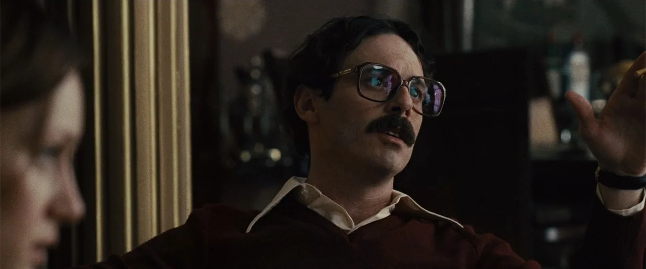 Argo (2012) movie still: medium — An interior space with warm lighting and period-appropriate decor in a domestic setting. A man in a maroon sweater…