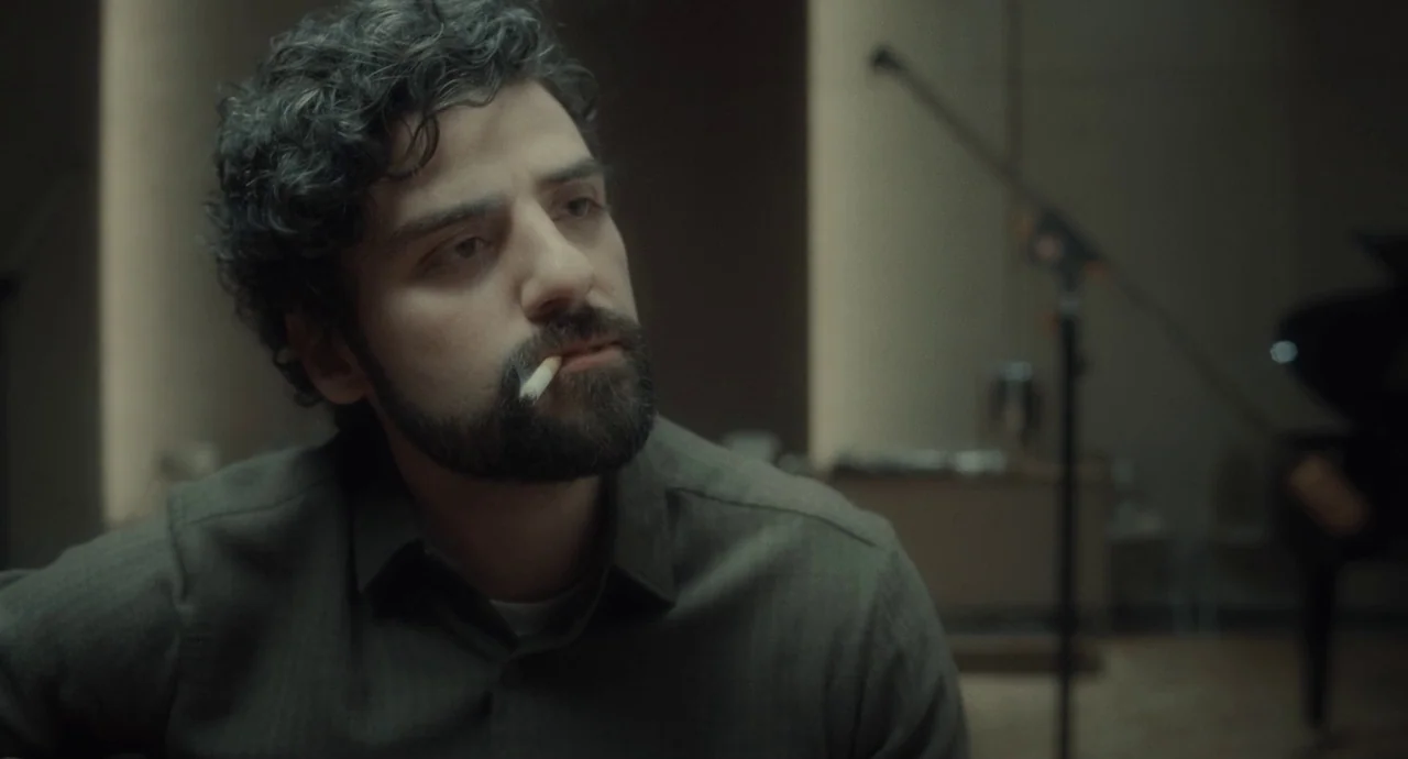 Inside Llewyn Davis (2013) movie still: medium — A dimly lit recording studio features a man sitting in the foreground. He is holding a guitar and…