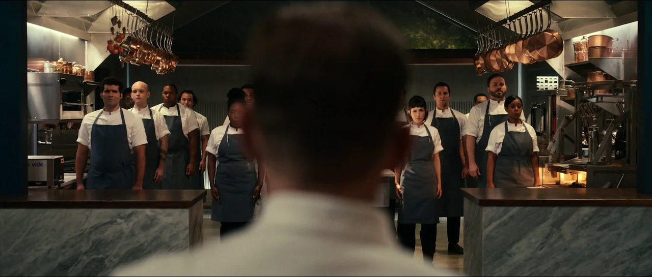 The Menu (2022) movie still: medium — A pristine professional kitchen features marble countertops and hanging copper cookware in the background. A…