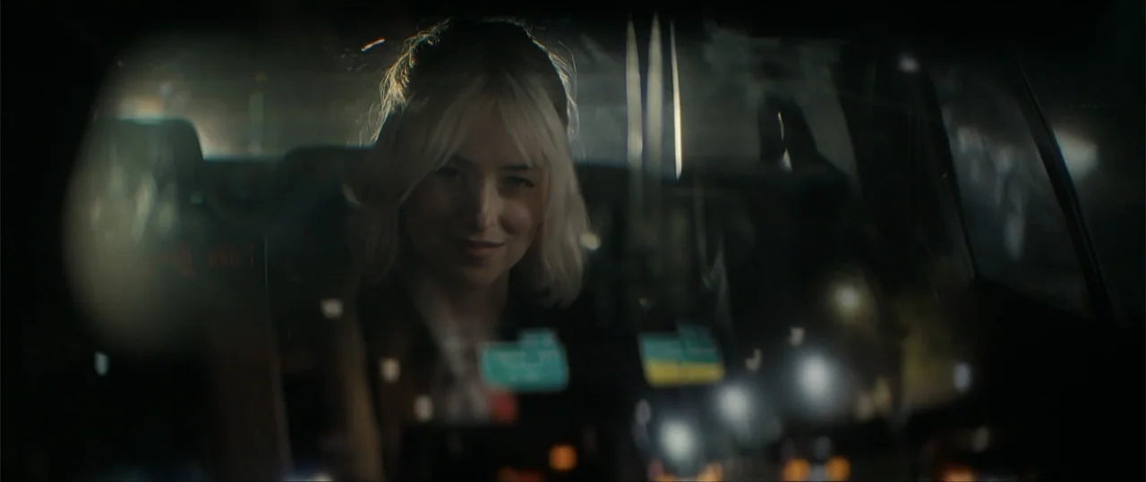 Daddio (2024) movie still: medium — A woman sits inside a car at night, viewed through the windshield glass. Reflections of dashboard lights and the…