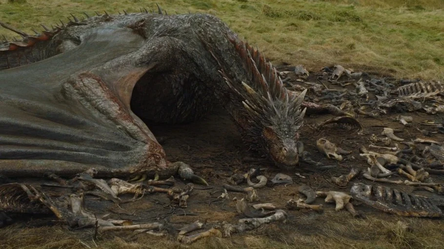 Game of Thrones (2015) movie still: wide — An open grassy field contains a large dragon lying beside scattered animal bones. The creature rests its…