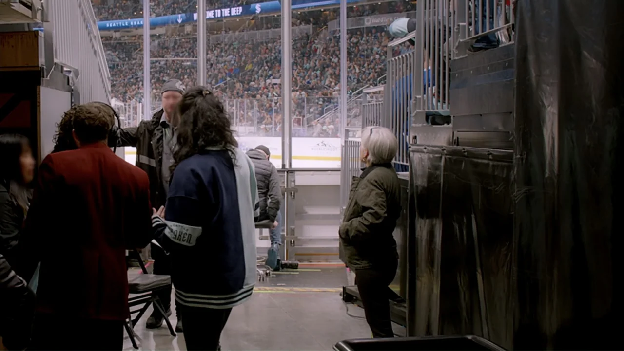 Jack in Time for Christmas (2024) movie still: medium — A concrete corridor beneath the stands of a large professional hockey arena. Several people…