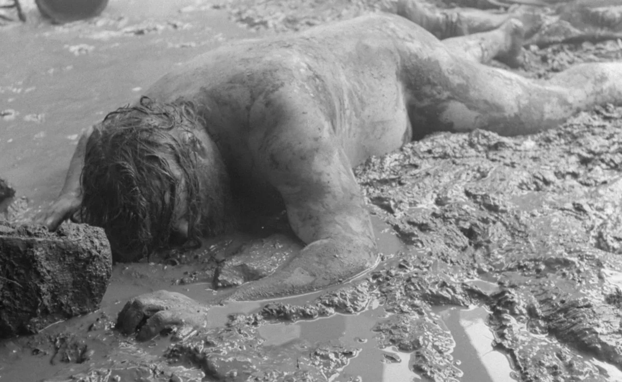 Hard To Be A God (2013) movie still: medium — A man lies prone in a thick patch of wet, deep brown mud. He is completely uncovered and his face is…