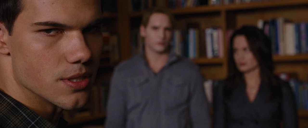 The Twilight Saga: Breaking Dawn – Part 1 (2011) movie still: closeup — A wooden room with rows of books lining the wall in the background. A man…