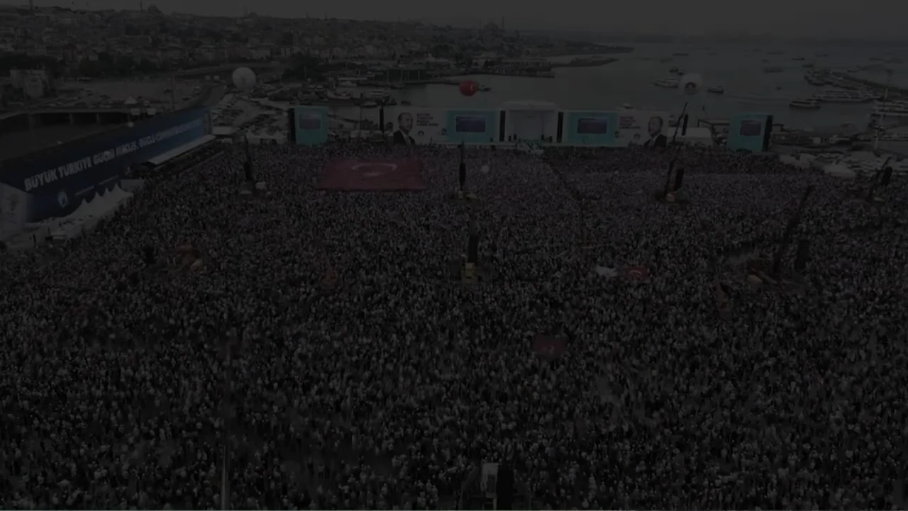 A Gift from God (2019) movie still: establishing — A massive crowd fills a large coastal square in front of the water. Several large screens and…