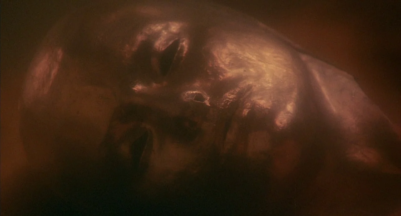 Conquest (1983) movie still: closeup — An abstract, dark space contains a single metallic, human-like mask. The object occupies the frame against a…