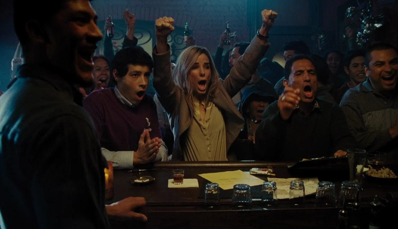 Our Brand is Crisis (2015) movie still: medium — A dimly lit tavern with a wooden counter and scattered glassware. A diverse group of people…