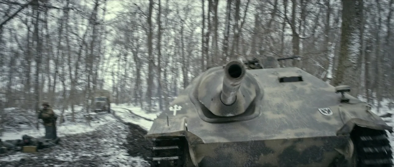 Battle of the Bulge (1965) movie still: medium — A snowy forest path is framed by leafless trees and patches of melting ice. A military tank moves…