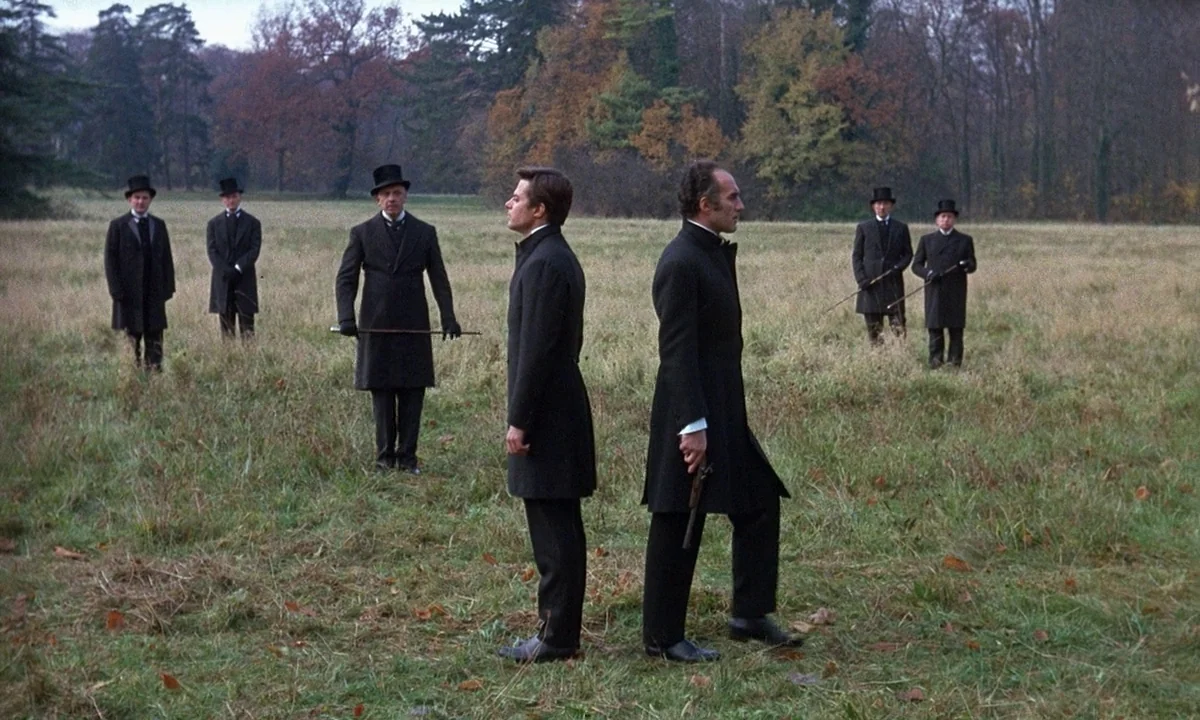 Belle De Jour (1967) movie still: fullbody — An open grassy field in autumn surrounded by dense trees under an overcast sky. Two men in period black…