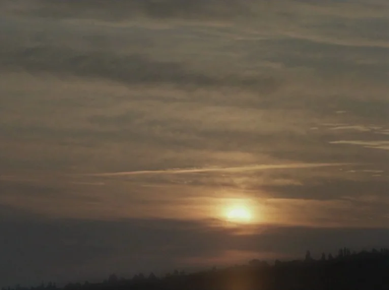 Hail Mary (1985) movie still: establishing — A vast sky is filled with layered clouds during a low sun transition. The horizon line shows a…