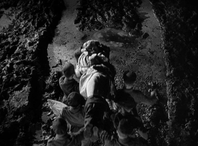 All Quiet on the Western Front (1930) movie still: wide — A group of soldiers moves through a deep, wet, and muddy trench system. They are…