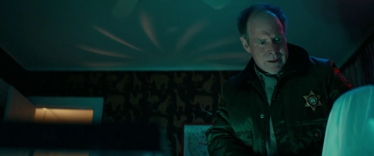 Halloween (2018) (2018) movie still: medium — An interior space features dark wallpaper with a gold animal pattern and a ceiling fan. A middle-aged…