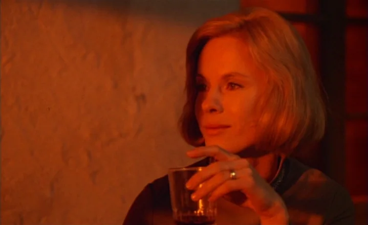 The Passion of Anna (1969) movie still: closeup — A room with textured wall surfaces lit by deep orange warm light. A blonde woman holds a glass…