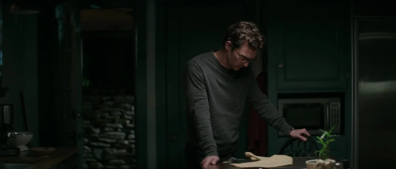 The Sea of Trees (2015) movie still: medium — A dimly lit room with dark green cabinetry and a stone exterior visible through doorway. A man in a…