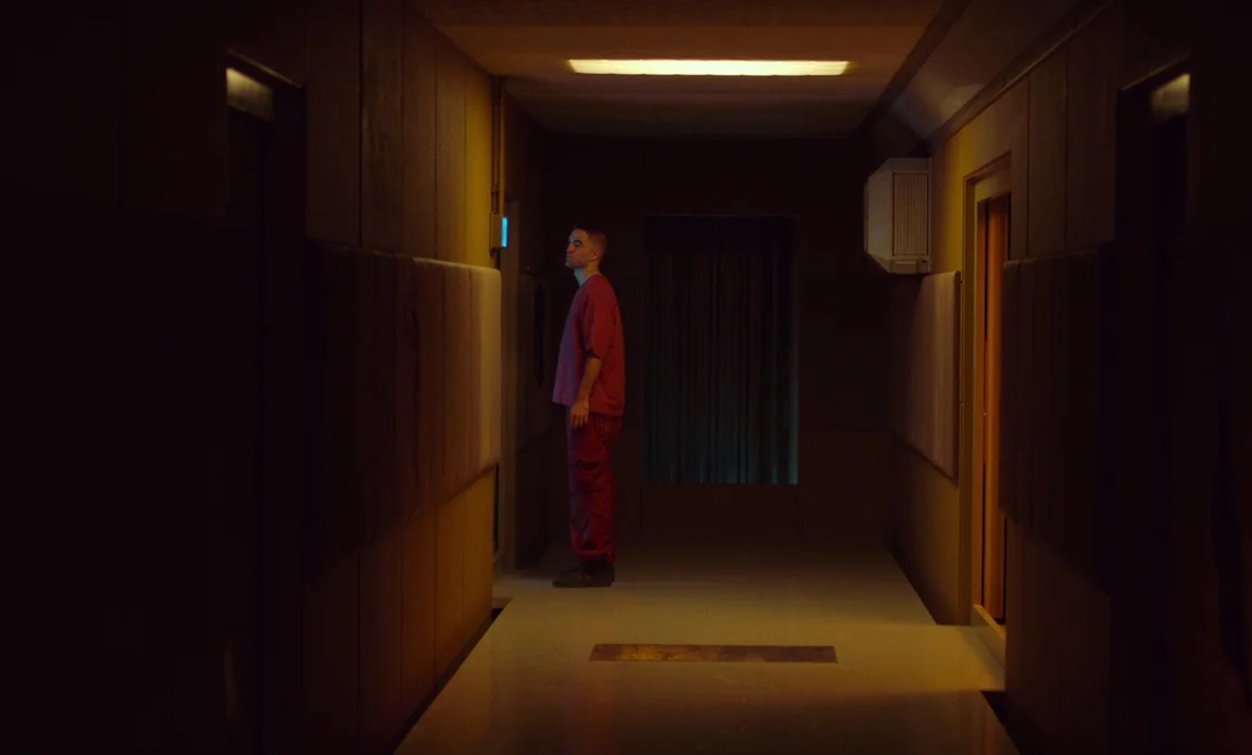 High Life (2018) movie still: fullbody — A dark, narrow corridor features paneled walls and a single rectangular ceiling light fixture. A man in a…