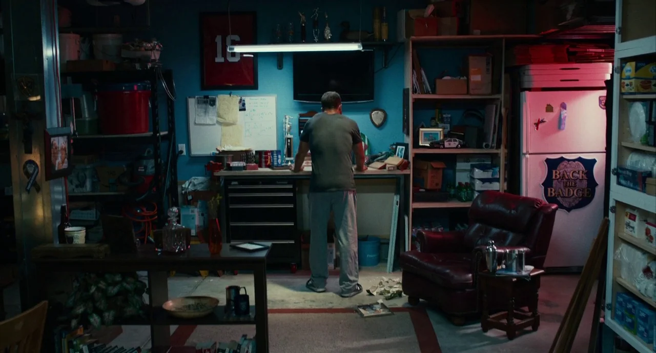 Blindspotting (2018) movie still: wide — A cluttered residential garage serves as a hobby space with storage shelves and equipment. A man stands at…