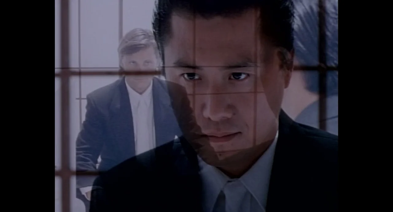 American Yakuza (1993) movie still: closeup — An interior space is divided by a window frame with a grid pattern. One man is foregrounded while…