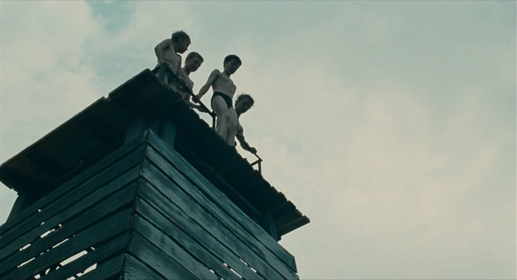 The Lord of The Rings: The Return of the King (2003) movie still: wide — A weathered wooden platform stands against an overcast sky. Four boys wait…
