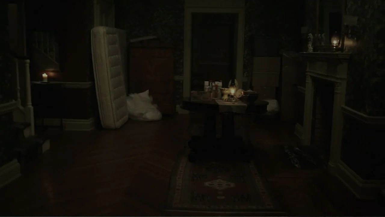 Silent House (2011) movie still: wide — A dark, dimly lit living room features Victorian wallpaper and antique furniture in disarray. A mattress…