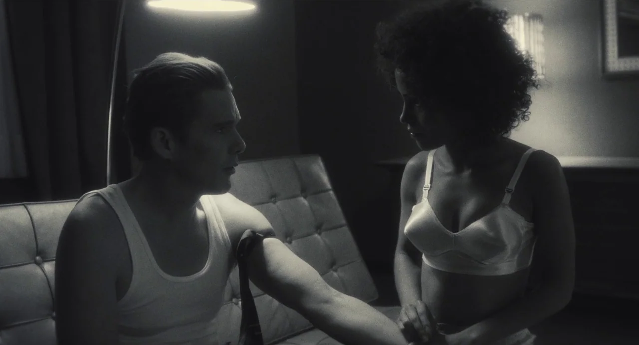 Born To Be Blue (2015) movie still: medium — A dimly lit room with a button-tufted leather couch and a wall-mounted light fixture. A man and woman…