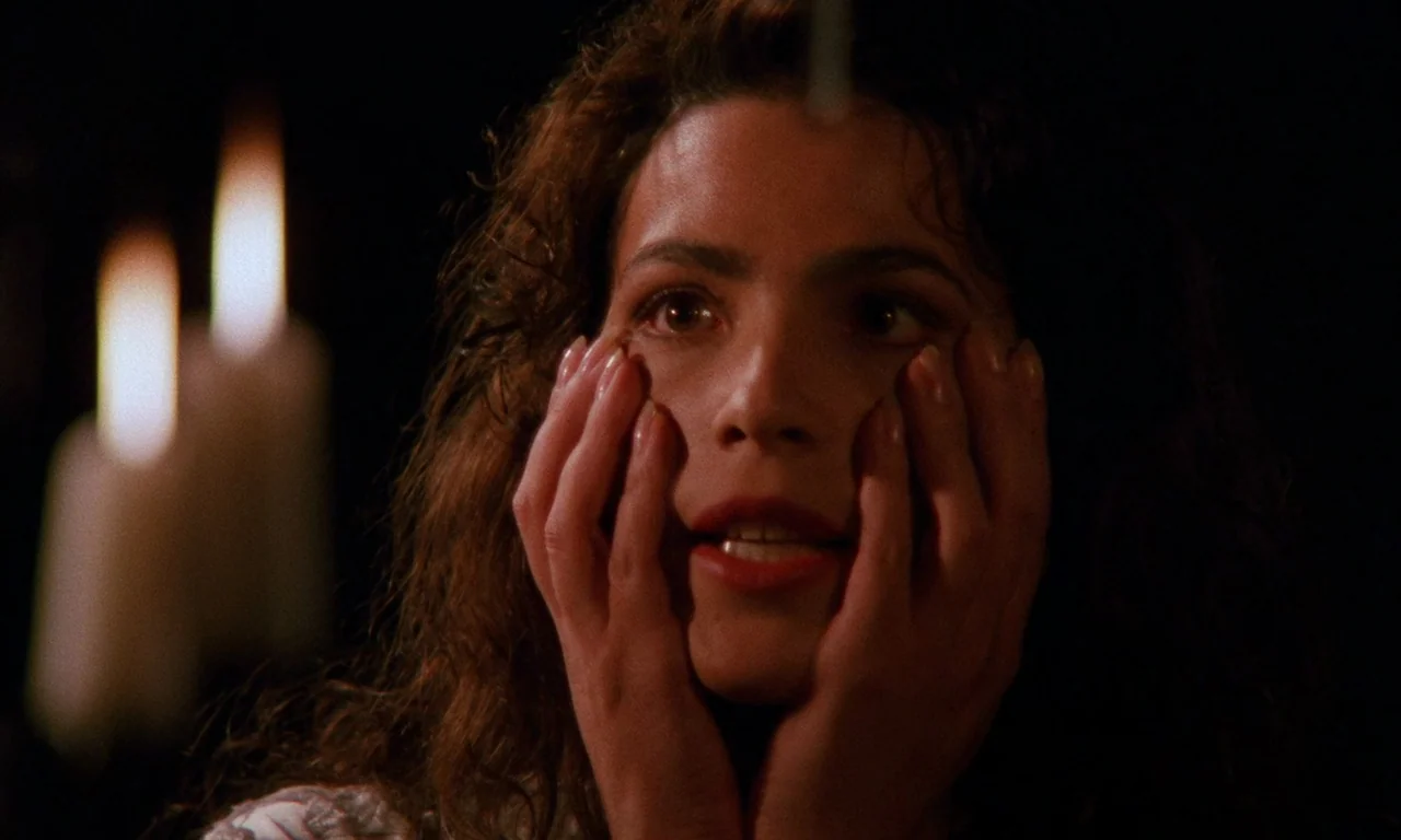 The Church (1989) movie still: closeup — A woman stands in a dark room illuminated primarily by nearby candlelight. She holds her face with both…
