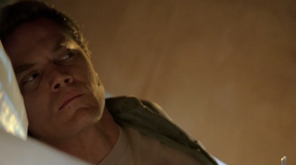 Bug movie still: closeup — A man lies on a pillow within a softly lit room at night. He gazes off to the side while resting his head.