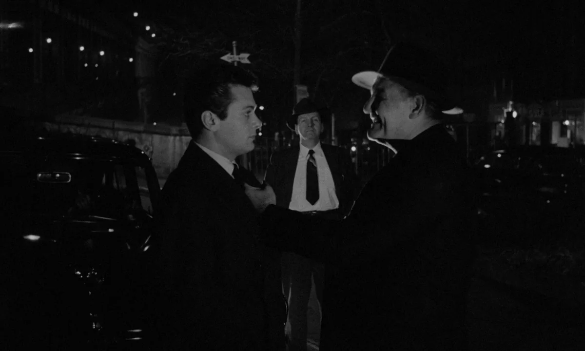 Sweet Smell of Success (1957) movie still: medium — A dark urban street at night featuring a vintage car and a street sign. An older man stands…