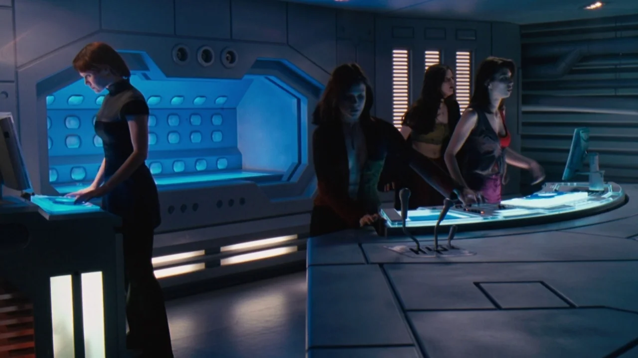 Jason X (2001) movie still: wide — A high-tech control deck features large glowing blue monitors and angular metal surfaces. Four women stand at…